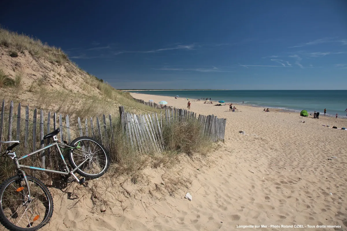 Accès à la plage du Bouil à Longeville-sur-Mer avec un vélo garé contre les ganivelles de la dune.